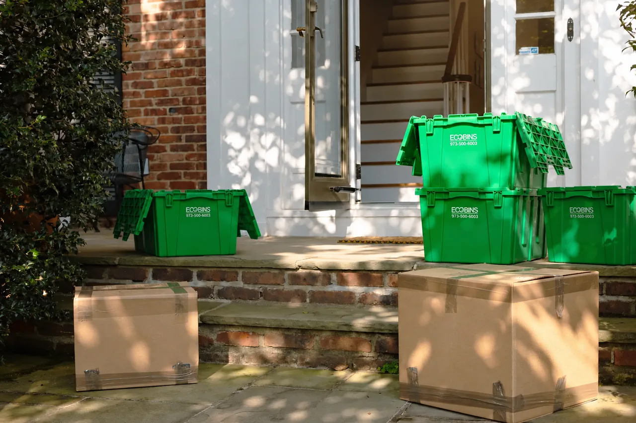Reusable green EcoBins beside taped cardboard moving boxes at a front door