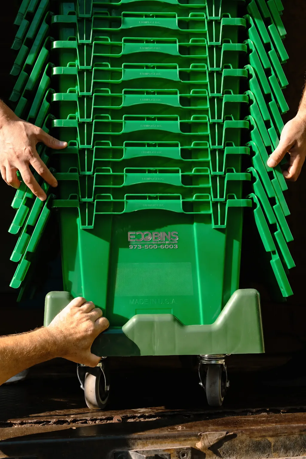 Empty green EcoBins nested together on a moving cart with their hinged lids open